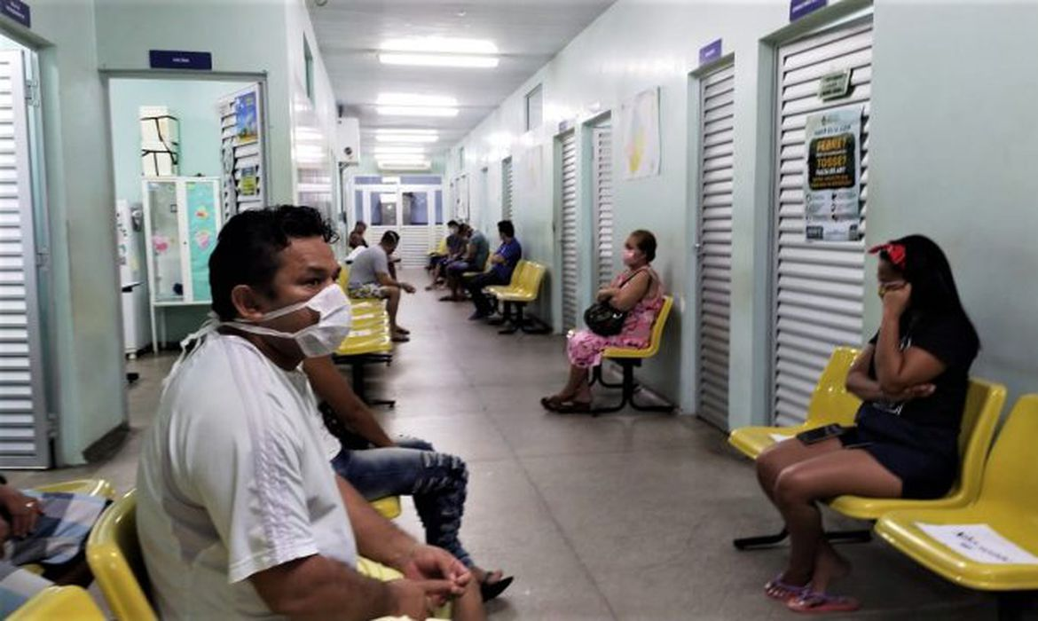 Pessoas usando máscara aguardam no corredor de uma unidade de saúde.