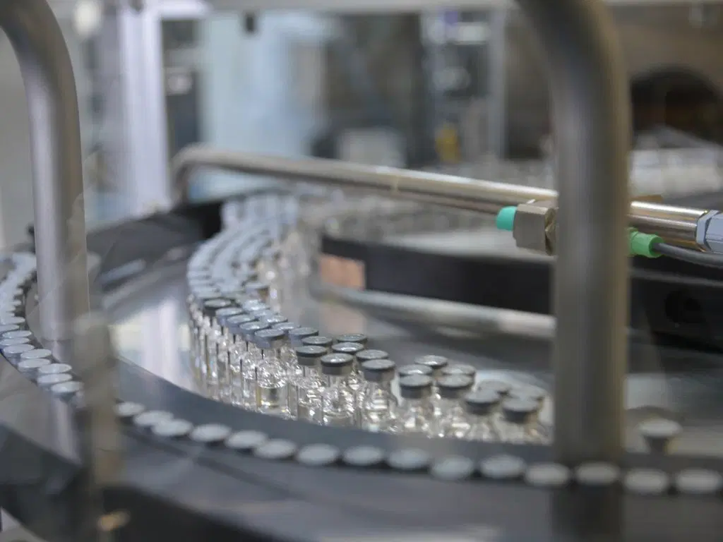 Frascos de vacinas em produção percorrendo uma máquina.