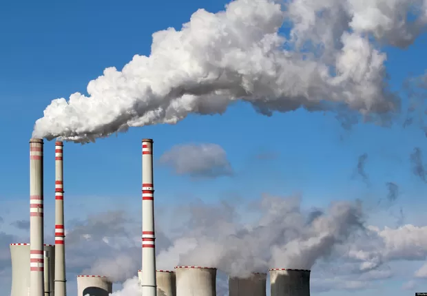 Imagem de chaminés de indústrias eliminando nuvens de gás branco no céu.