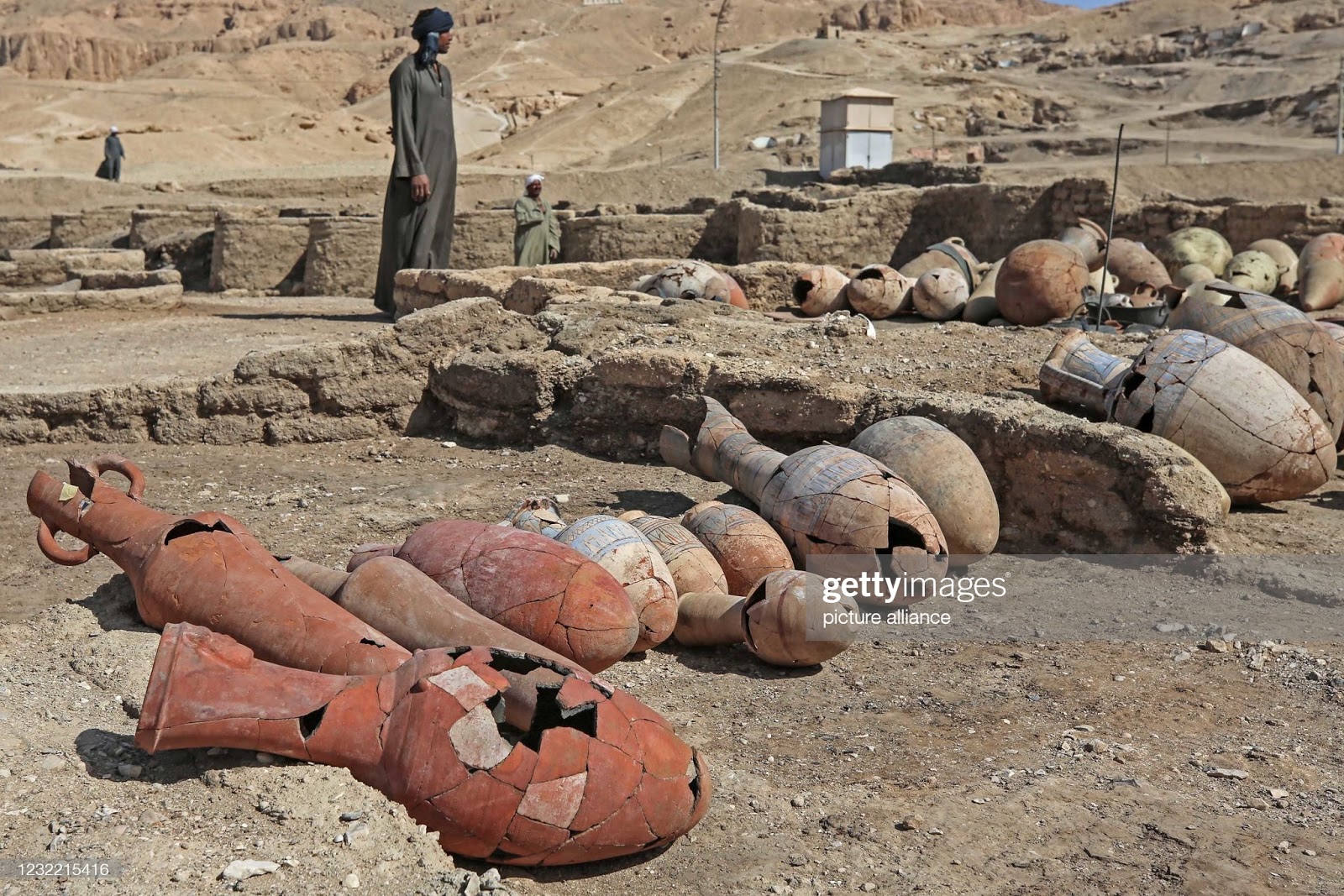 Vasos e recipientes de barro, de vários tamanhos e formas, enfieirados no chão do sítio arqueológico, sendo observados por um homem com roupas típicas da região.