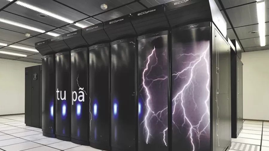 No centro de uma sala com paredes brancas e sem janelas, está o supercomputador Tupã, um grande bloco de metal preto, tão alto que quase alcança o teto, que comporta diversos equipamentos em seu interior.